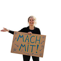 Eine Frau steht mit einem Schild vor der Kamera, auf dem „Mach mit” steht.