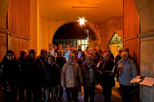 Der Kirchenchor St. Cäcilia Birkungen im Advent unter dem Torbogen des Pfarrhauses. Beleuchtet wird die Toreinfahrt von einem Stern über dem Chor.